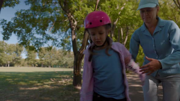 Parent Mother Teaches Girl Child In Pink Helmet Roller Skating