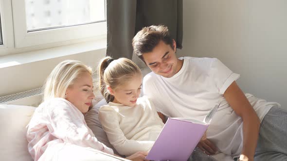 Portrait of Happy Family Reading a Book Together on Bed