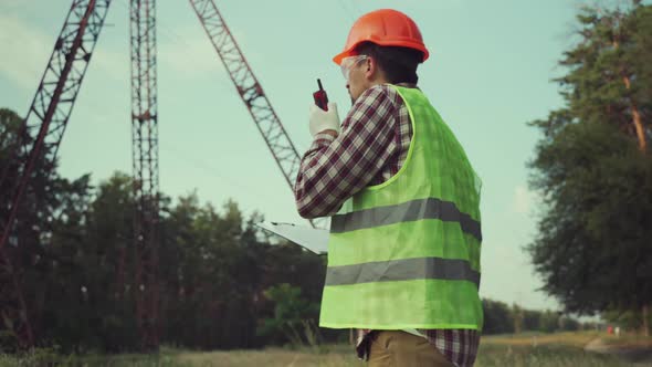 Electrical Engineer Wearing Hard Hat and Safety Vest Checking Electrical Systems on High Voltage