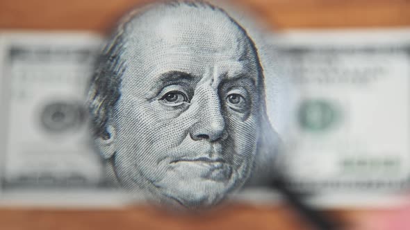 One Hundred Dollars Inspects Under Magnifying Glass on Wooden Table