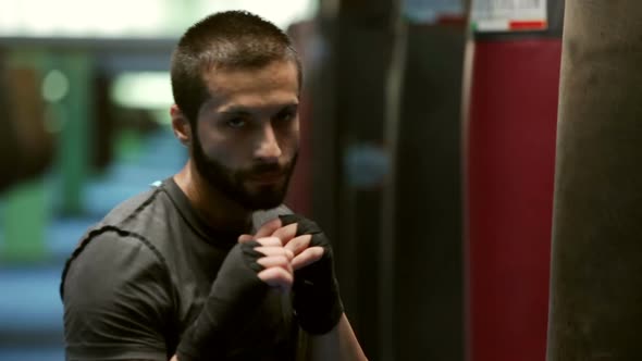 Young Sweaty Boxer is Warming Up Near Punching Bag in Gymnasium