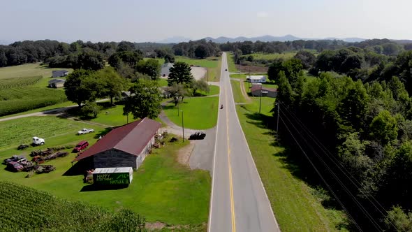 Aerial view of country road with cars commuting with cornfields and trees surrounding on a nice sunn