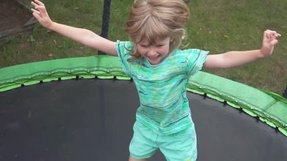 Cheerful Girl in Turquoise Tshirt is Jumping and Waving Hands on the Trampoline