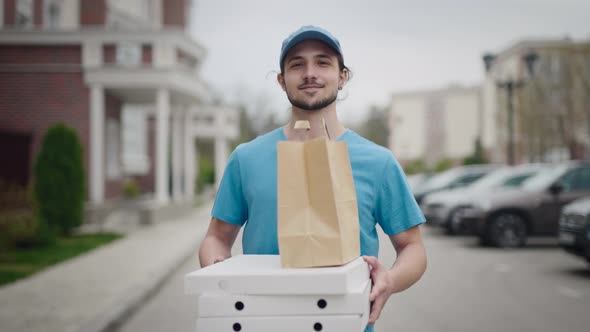 A Young and Energetic Delivery Man Carrying a Pizza and a Bag of Groceries