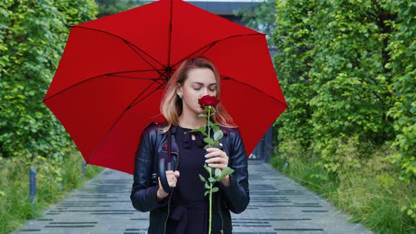 Upset Girl Stands Under Umbrella with Red Rose