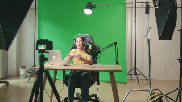 Asian Kid Girl Holding Mobile Phone And Talking To Camera While Live Stream On Green Screen