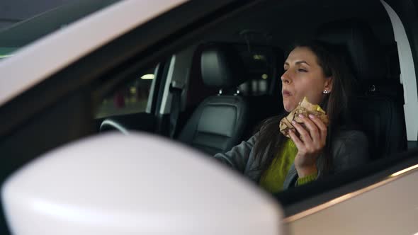 Woman Eating Sandwich Sitting in the Car on the Parking