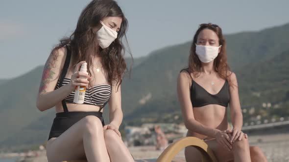 Two Diverse Beautiful Women Using Medical Face Mask Applying Sun Cream on Skin on the Beach