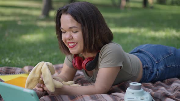 Relaxed Positive Little Woman Playing with Toy Lying on Blanket in Spring Summer Park