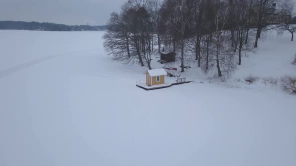 Zoom out aerial footage with close up view at beginning showing tiny fishing hut and cabin while rev