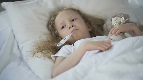 Sick Little Girl Lying in Bed Sad With Thermometer in Mouth, Kid Caught Cold