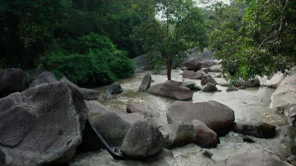 Drone view of creek flowing between large rocks in a tropical forest landscape