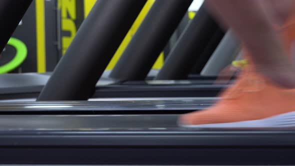 A Fit Woman Starts To Run on a Treadmill in a Gym - Side Closeup on the Feet