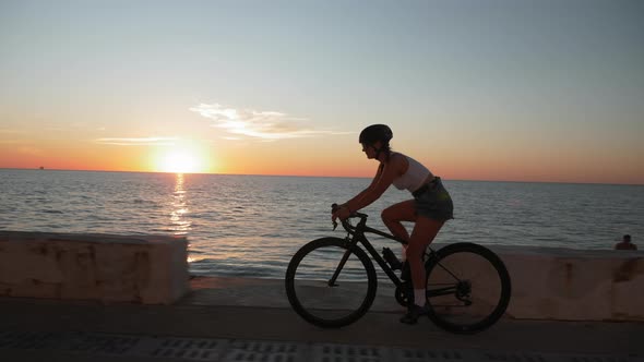 Young motivated woman in top and shorts is cycling on promenade at sunset. Cycling concept