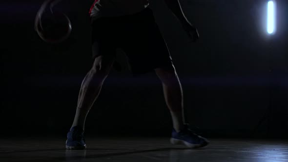 A Man with a Basketball on a Dark Basketball Court Against the Backdrop of a Basketball Ring in the