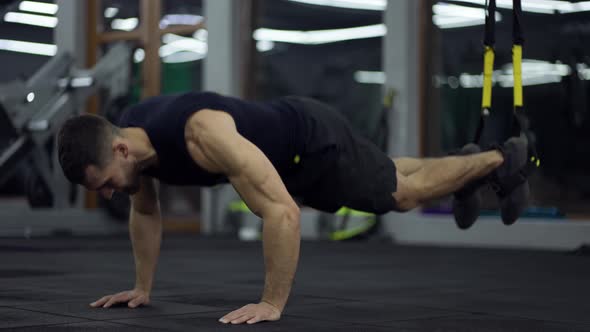 Sportsman Doing Flooring Abs Exercises with TRX Straps at Gym