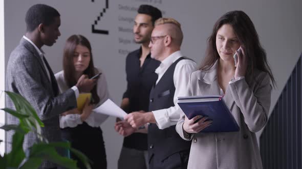 Brunette Caucasian Young Woman Hanging Up Phone and Looking at Camera Standing in Office Corridor