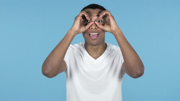 Young African Man Searching with Handmade Binoculars, Blue Background