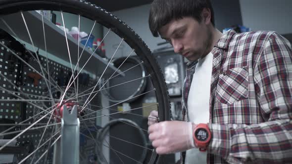 A Technician Adjusts Bicycle Spokes and Repairs a Wheel in a Bike Store Workshop