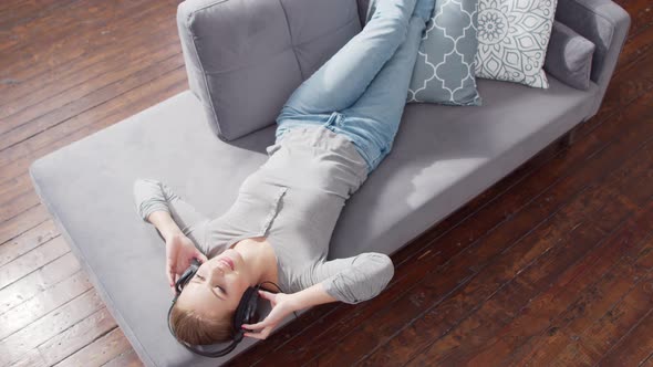 Young beautiful girl lies on a sofa in headphones