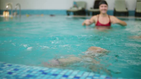 Young Mother is Showing to Her Little Son to Dive Under Water in the Swimming Pool While He is