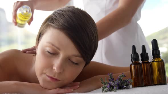 Masseur pouring massage oil on the back of her patient