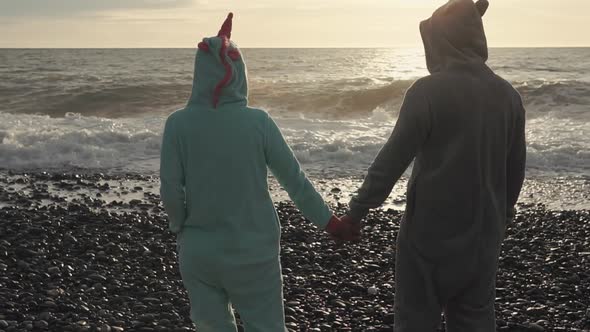 Man and Woman in Kigurumi Are Standing on a Beach and Looking on Ocean Waves