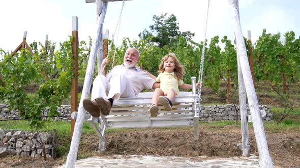 Happy Family of Grandchild and Grandfather Enjoy Swinging Together in Backyard Swing