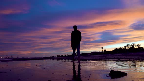 Espladas man walks towards the horizon over the water on a beautiful beach with an incredible sunset