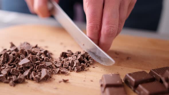 Woman Chopping Black Dark Chocolate on Wooden Cutting Board