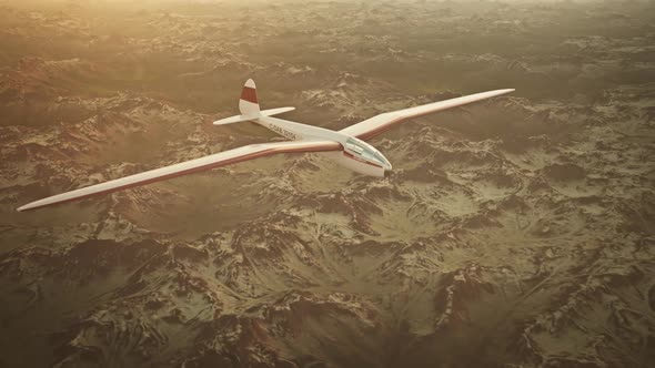 The white sailplane calmly gliding in the sky over the snow-covered mountains.