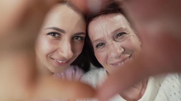 Happy Elderly Mother and Adult Daughter Look Through the Heart