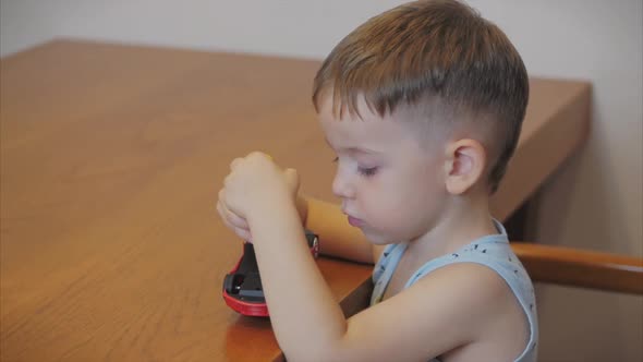 Shooting a Portrait of a Cute Preschool Boy, the Child Repairs His Favorite Red Toy Car for Kids