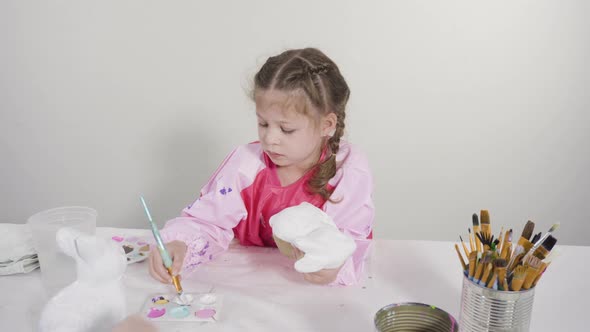 Little girl painting paper mache figurine at homeschooling art class.