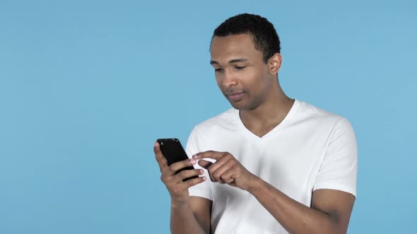 Young African Man Excited for Success While Using Smartphone Blue Background