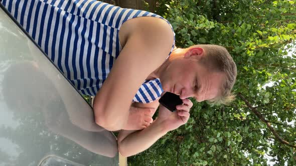 a Young Man in a Striped Tshirt Vest Talking on the Phone Leaning on a Car