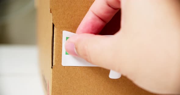 Hands applying MADE IN IRELAND flag label on a shipping cardboard box with products. Close up shot w