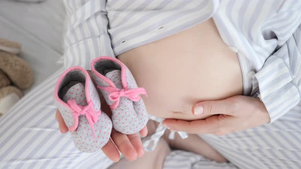 Baby Shoes In The Hands Of A Future Mother. Pregnant Belly Closeup