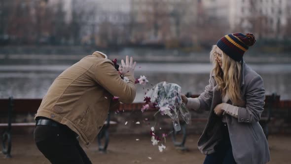 Crazy Caucasian Girl Taking Bouquet of Flowers and Brutally Hiting Guy on River Embankment