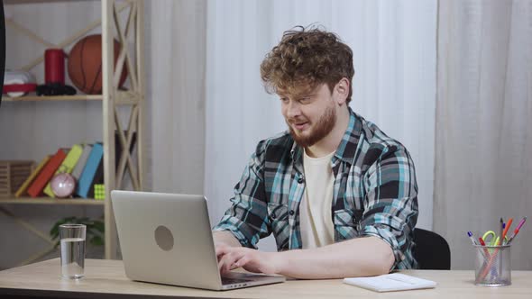 Young Man in Checkered Shirt Typing on Laptop Keyboard and Enjoying Good News or Deal