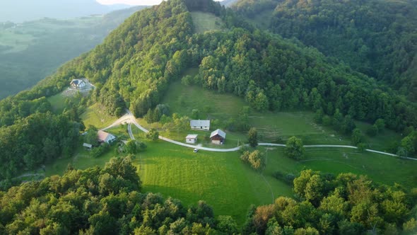 House Structures At The Meadow On The Hilltop Surrounded With Thick Green Forest . aerial