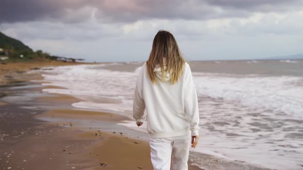 Blonde Woman Walking Along Ocean Coast Alone Rear View