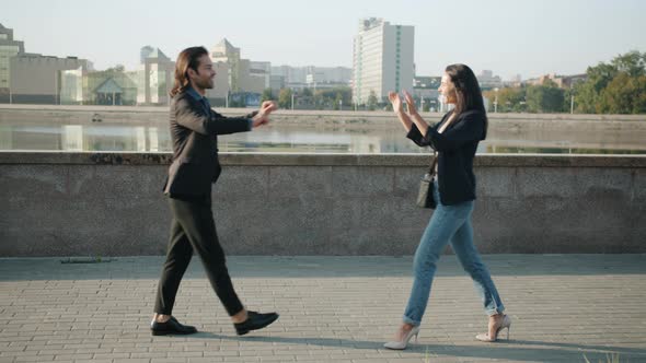 Cheerful Young Man and Woman Walking Outdoors Along River Embankment Doing Highfive Smiling