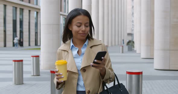 Businesswoman with Takeaway Coffee Walking to Office Looking at Mobile Phone