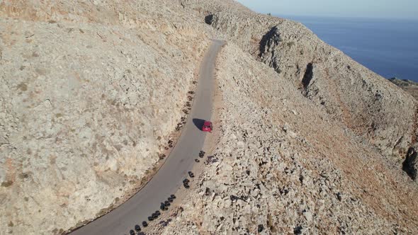 Aerial drone shot of Red car driving along the narrow coastal road above rocky shore