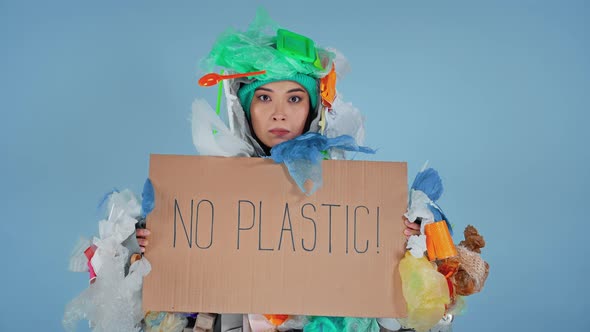 Woman dressed in the rubbish costume. Holding cardboard with inscription no plastic.