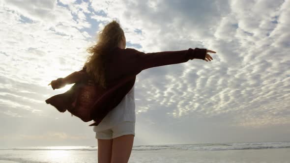 Rear view of young woman with arms outstretched looking at sea on the beach 4k