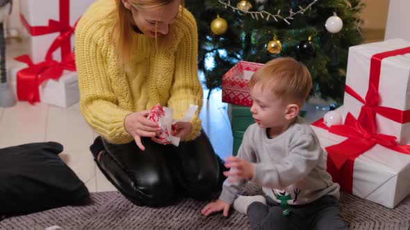 Happy mother having fun and playing together with her son near Christmas tree at home.