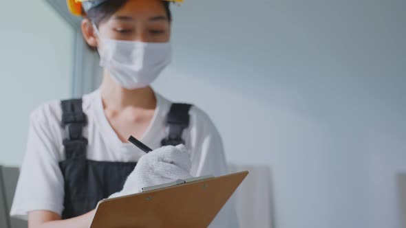 Asian construction worker girl wear face mask work to examine and check renovation in house.