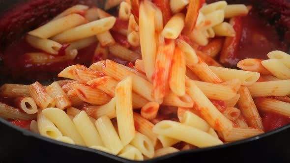 Stir pasta and tomato sauce in pan, close up